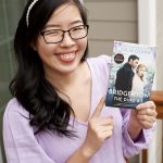 An Asian woman wearing a lilac shirt and pearl headband holding the first book of Bridgerton Series "The Duke and I" by Julia Quinn.